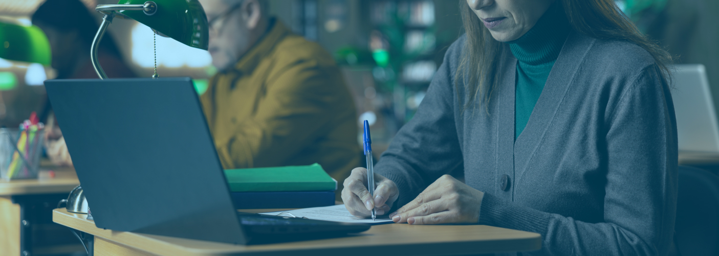 University admin working at a desk with a laptop and pen and paper